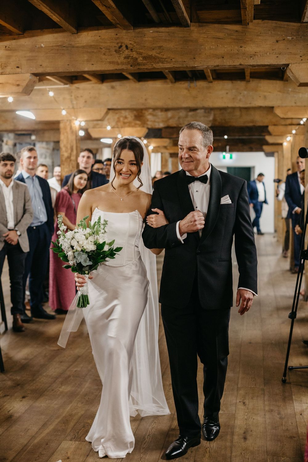 Bride walks down aisle with father in elegant rustic barn wedding ceremony.