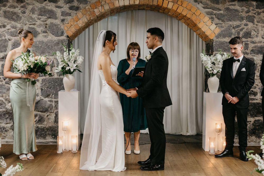 Bride and groom exchange vows at stone arch altar with white floral arrangements.