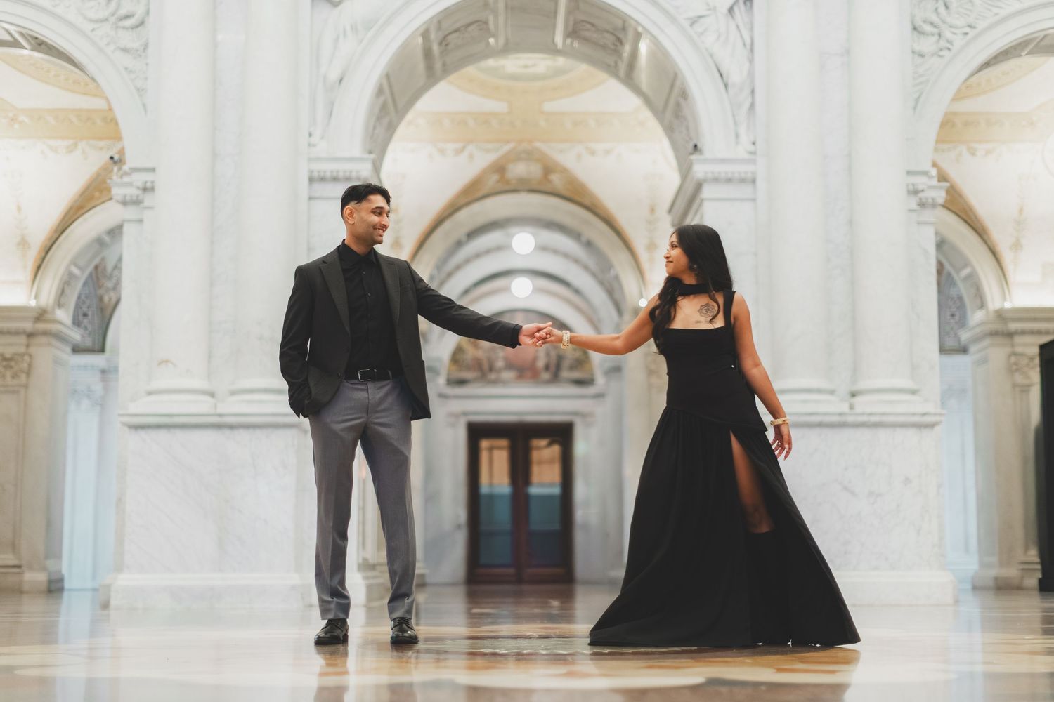 Elegant couple in black formal attire holding hands in a playful pose for their engagement session in dc a the library of congress