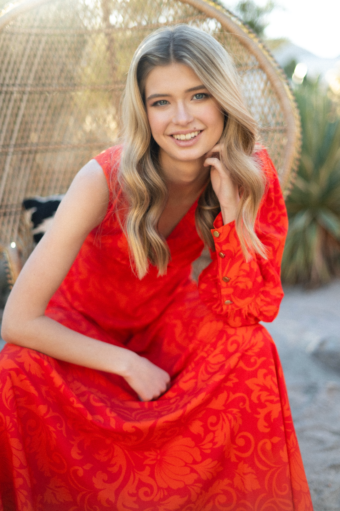 Blonde woman in a pink floral tiered maxi dress standing in a green field at sunset.