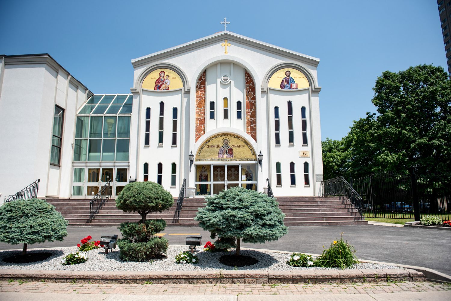 Exterior view of a white Orthodox church with mosaic icons and manicured landscaping on a sunny day.