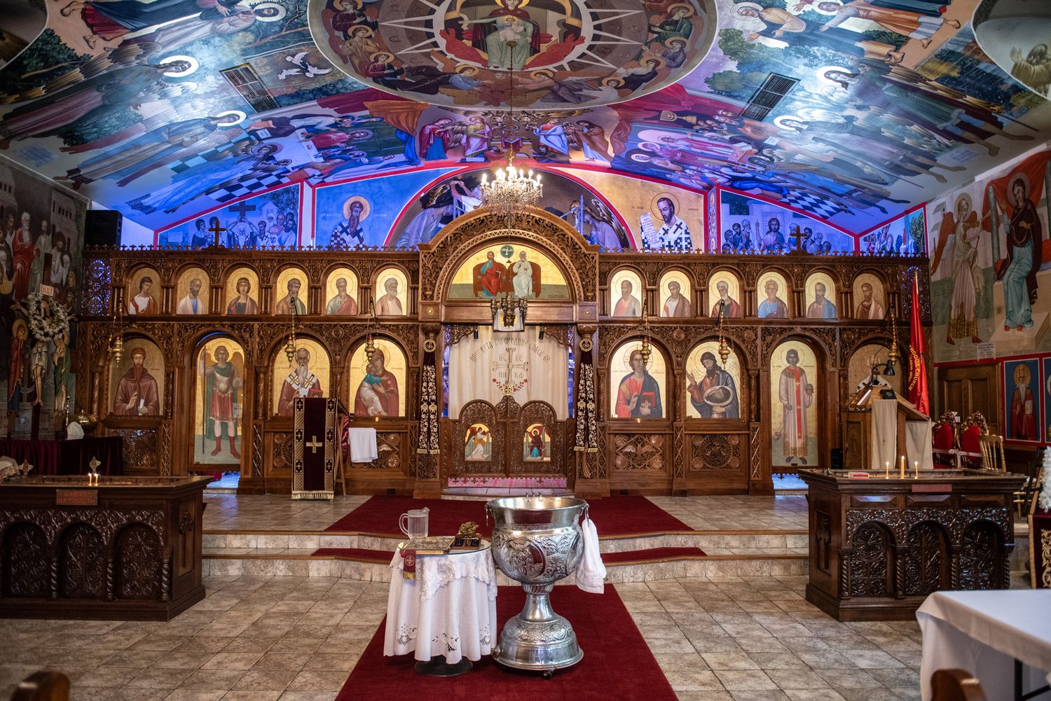 Ornate Eastern Orthodox church interior with iconostasis, baptismal font, and colorful ceiling frescoes.