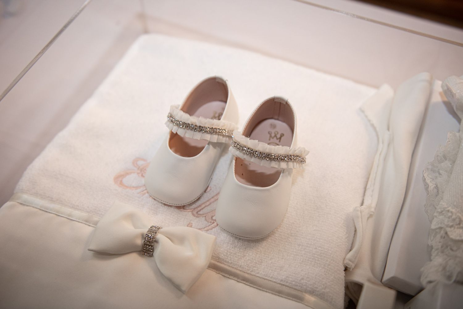 White baby baptism shoes with rhinestone bow detail displayed in gift box with white accessories.