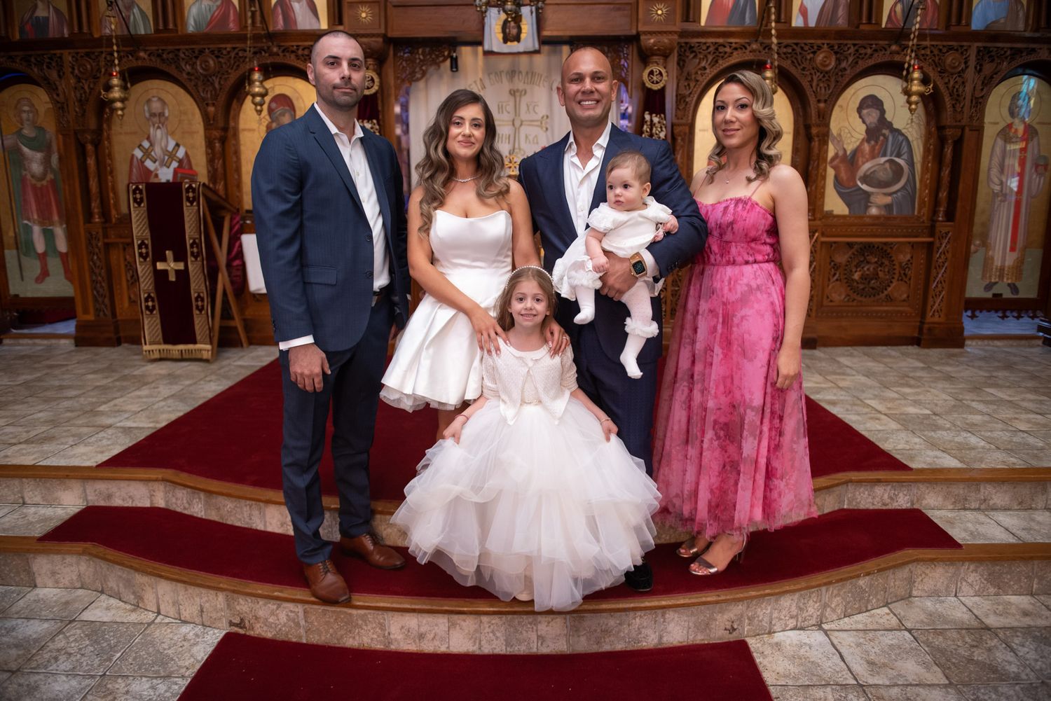 Family group photo on church steps with baby in baptism outfit, young girl in white tulle dress.