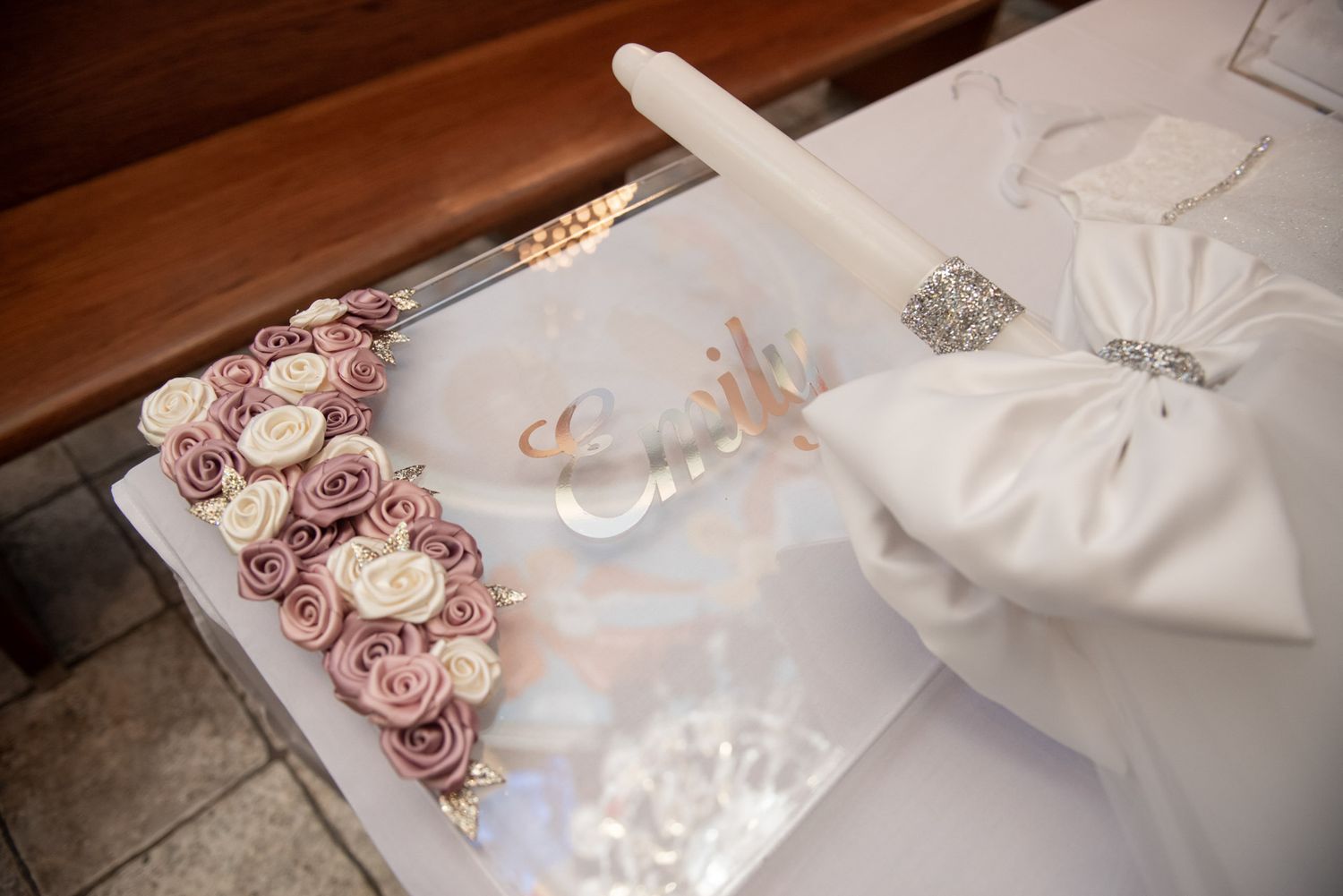 Baptism candle and personalized floral gift box with name Emily displayed on church pew.