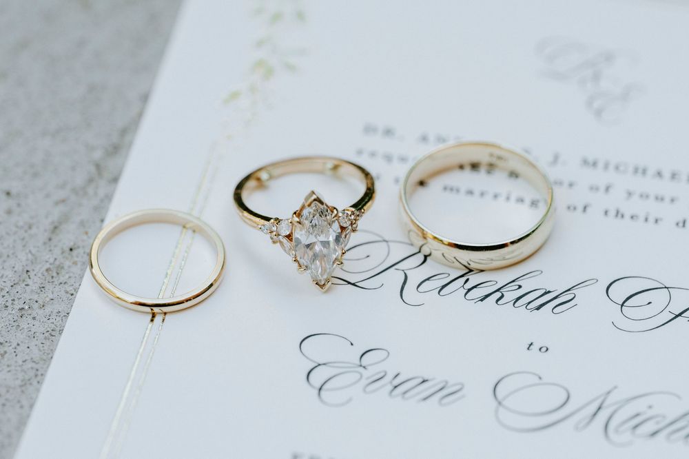 Gold wedding ring set with marquise diamond engagement ring displayed on elegant wedding invitation.