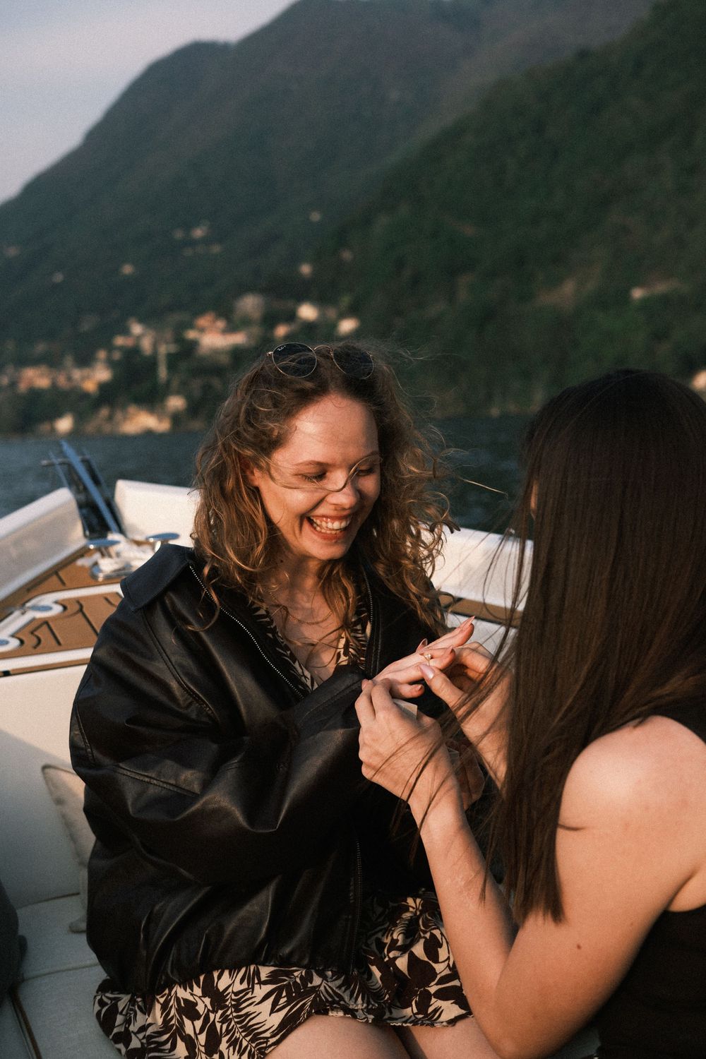 Two women sharing a joyful moment on a boat with scenic mountain lake views in the background.