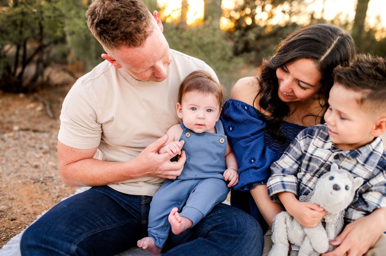 Happy family of four with two young children sitting together outdoors in warm golden light.