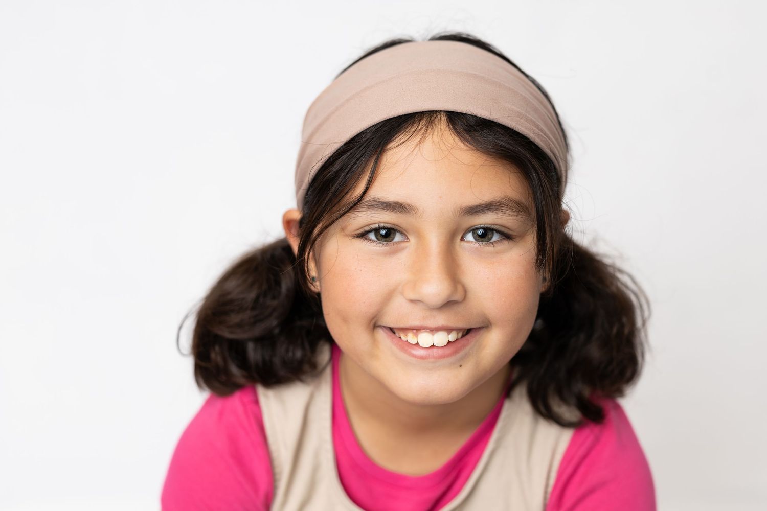 Smiling young girl with long brown hair and a braid, wearing a pink top, posing for a portrait photo.