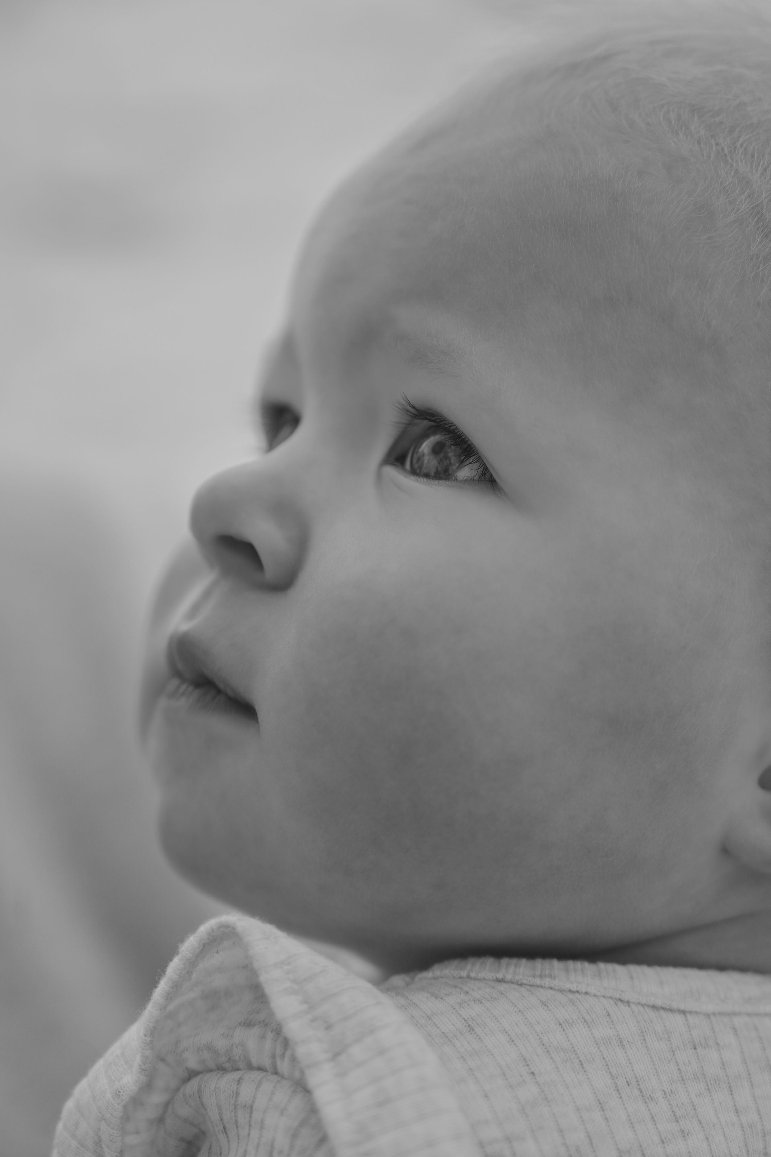 Black and white close-up portrait of a curious newborn baby looking upward with wide eyes.