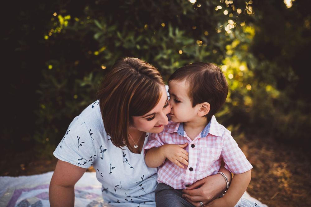 A couple shares an intimate moment in a sunlit garden setting wearing white and pink patterned clothing.