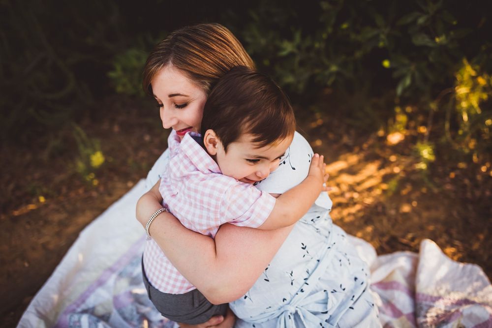 A mom and son moment captured during golden hour in a natural outdoor setting with soft sunlight filtering through trees.