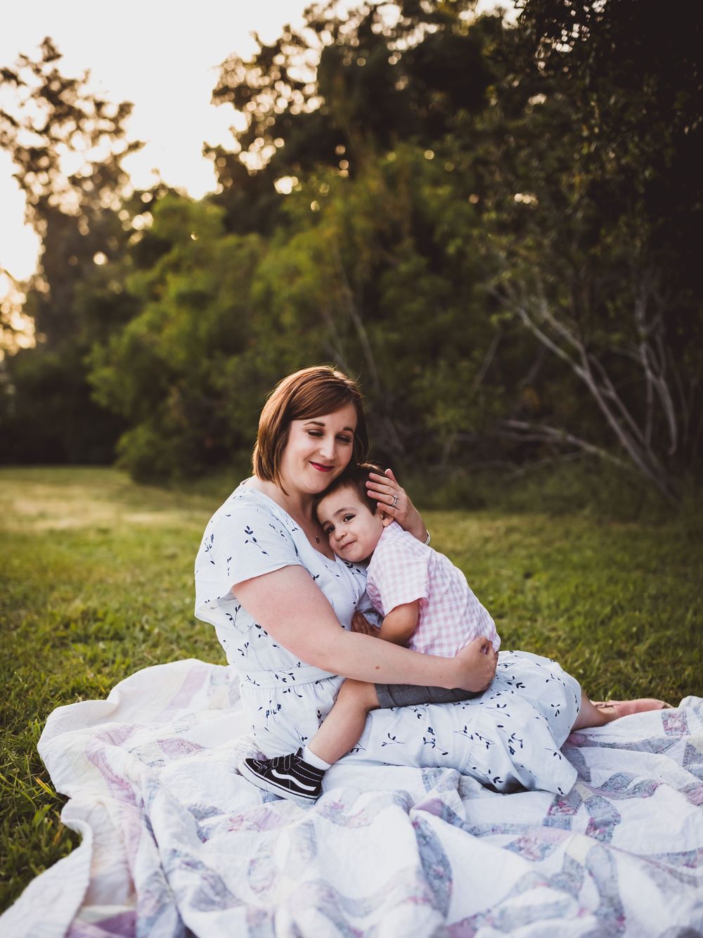 A tender moment captured on a white blanket in a sunlit grassy field during golden hour.