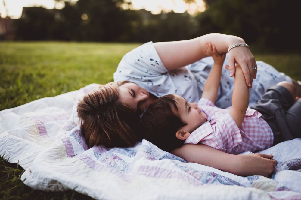 A mother and son share a tender moment while lying on a blanket outdoors during a photoshoot.