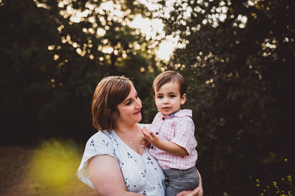 Mother and child share tender moment outdoors during golden hour sunset in nature setting.