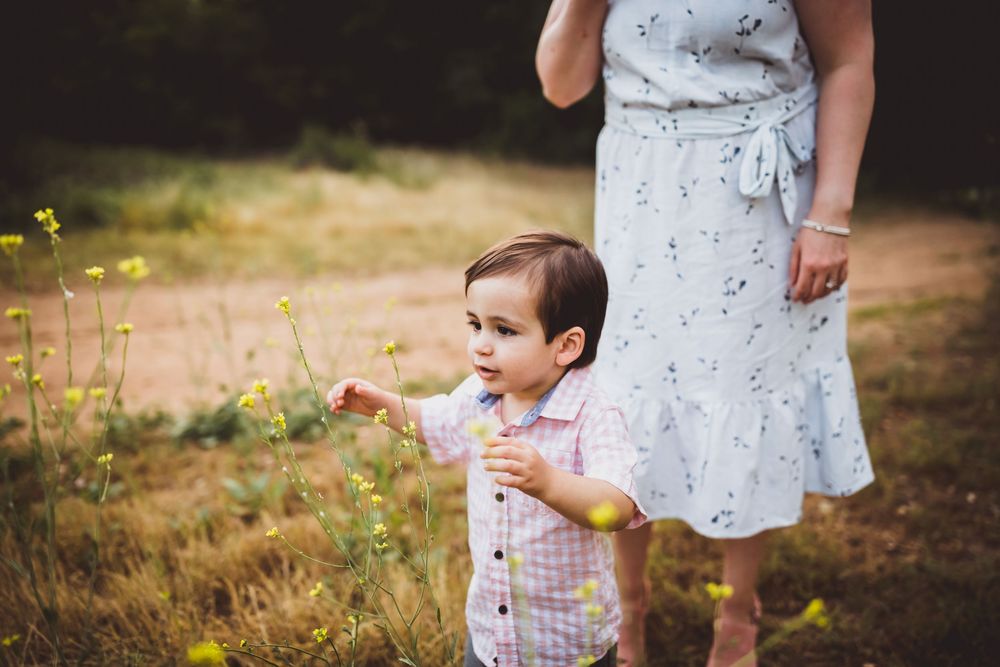 A child in a white dress explores a sunlit meadow with wildflowers at golden hour.