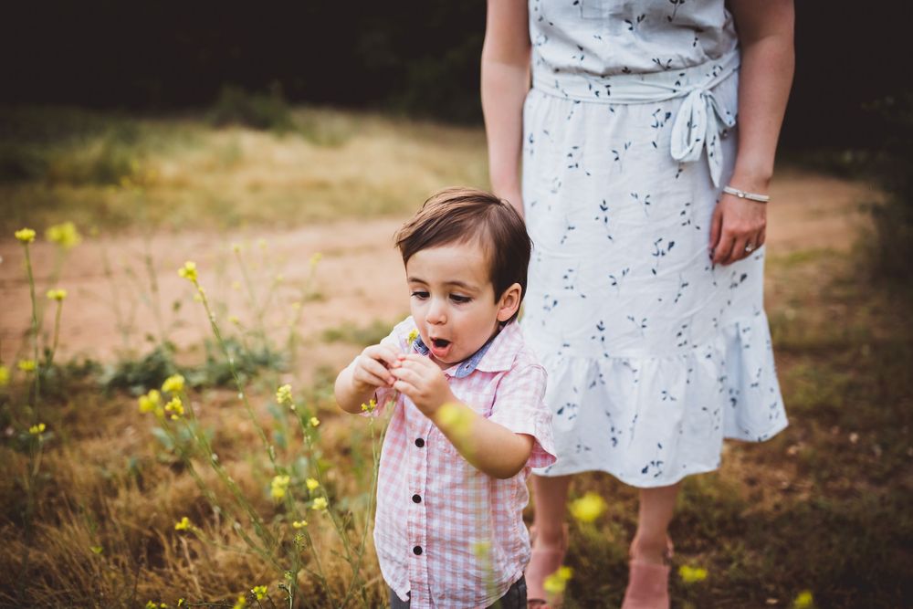 Mother and child in matching white outfits walk through sunlit field during family photo session.