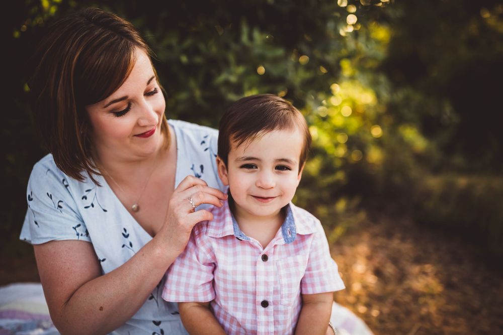 A parent and child share a tender moment outdoors in warm sunlight during a portrait session.