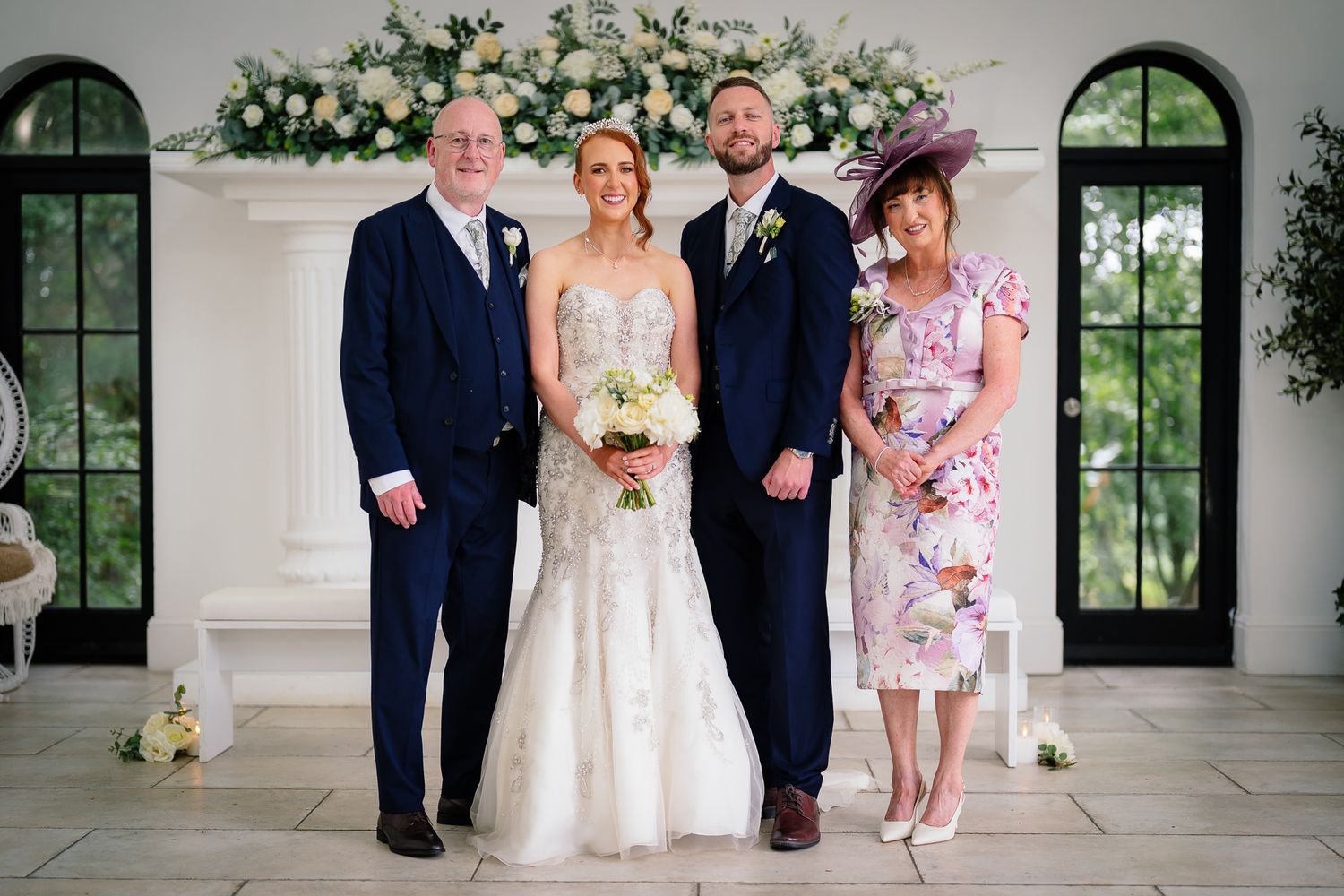 Elegant wedding party poses in front of white pillars and arched windows. Woodhill Hall.