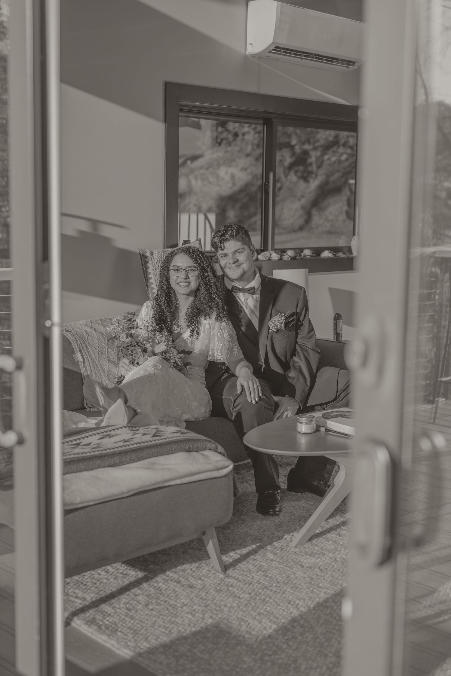 Black and white photo of people relaxing together on a couch in a sunlit living room interior.