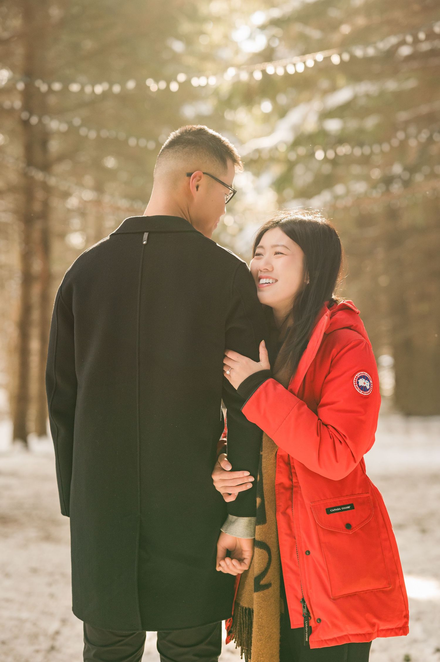 A couple embraces in a romantic moment against a white archway adorned with delicate pink cherry blossoms.