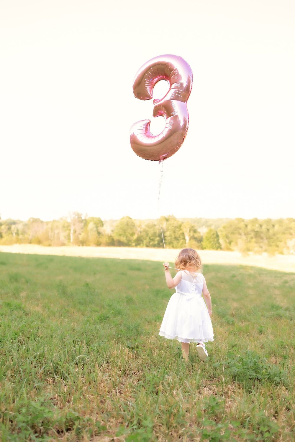 A small child in a white dress runs through a sunlit meadow on a warm summer day.