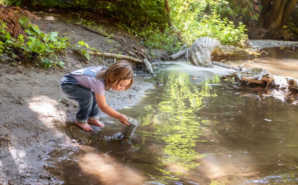 A child reaches down to touch flowing water in a natural outdoor setting.