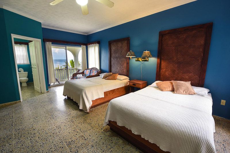Spacious beachfront bedroom with twin beds and blue walls overlooking the ocean.