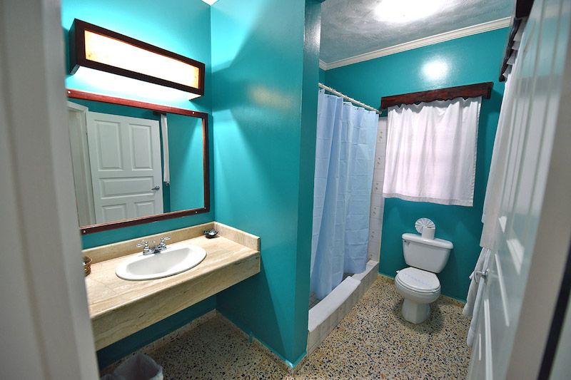 Modern turquoise bathroom featuring white fixtures, vanity mirror, and shower curtain.