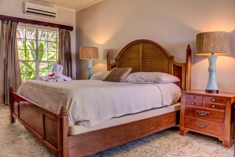 Elegantly furnished bedroom with wooden headboard, white linens, and tropical garden views.