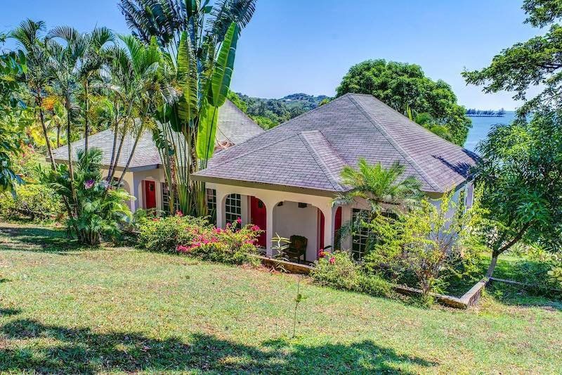 Tropical villa with red columns and stone roof nestled among palm trees on a hillside.