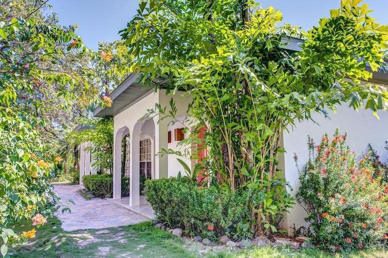 White villa exterior with arched colonnade walkway and flowering tropical garden.