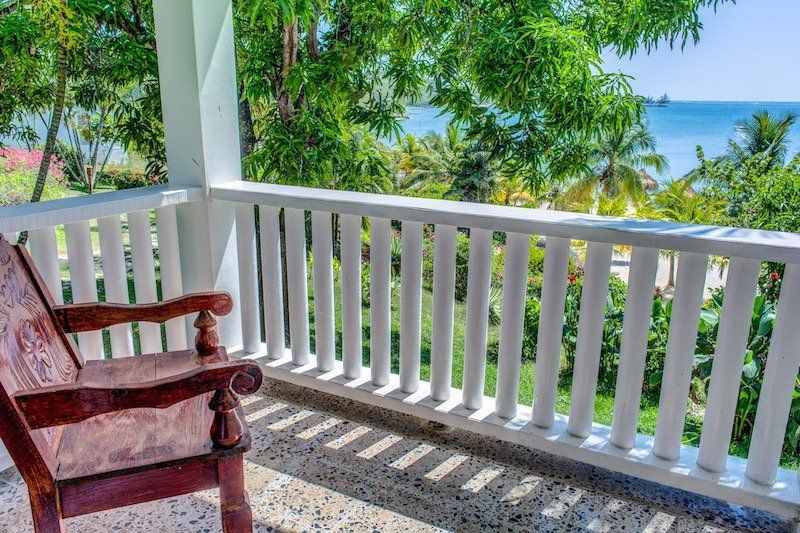 Wooden rocking chair on white balcony overlooking tropical ocean view.