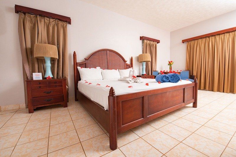 Spacious bedroom with wooden four-poster bed and beige curtains on tiled floor.