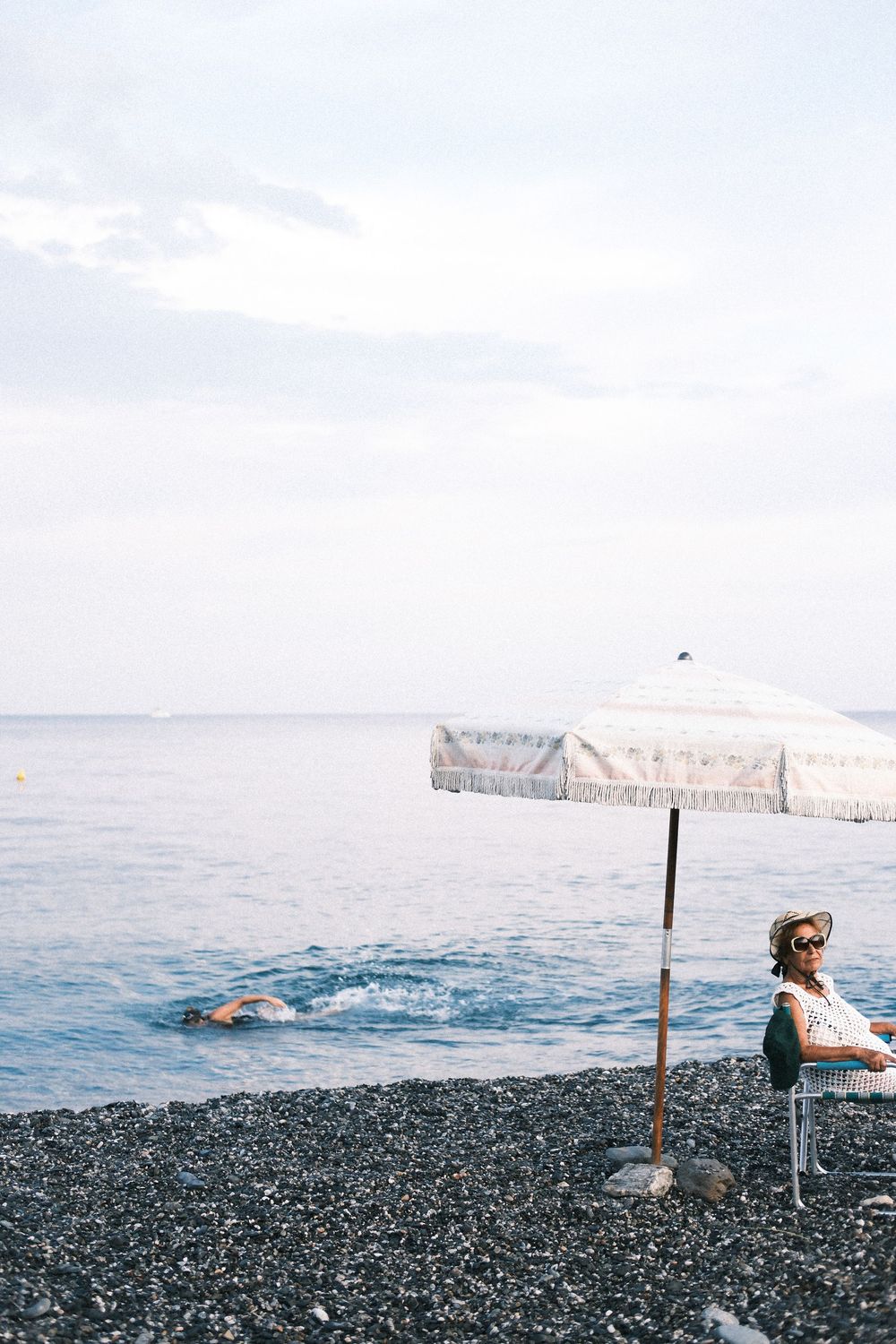 A series of connected photos showing someone lounging and swimming at a rocky beach with mountains in the background.