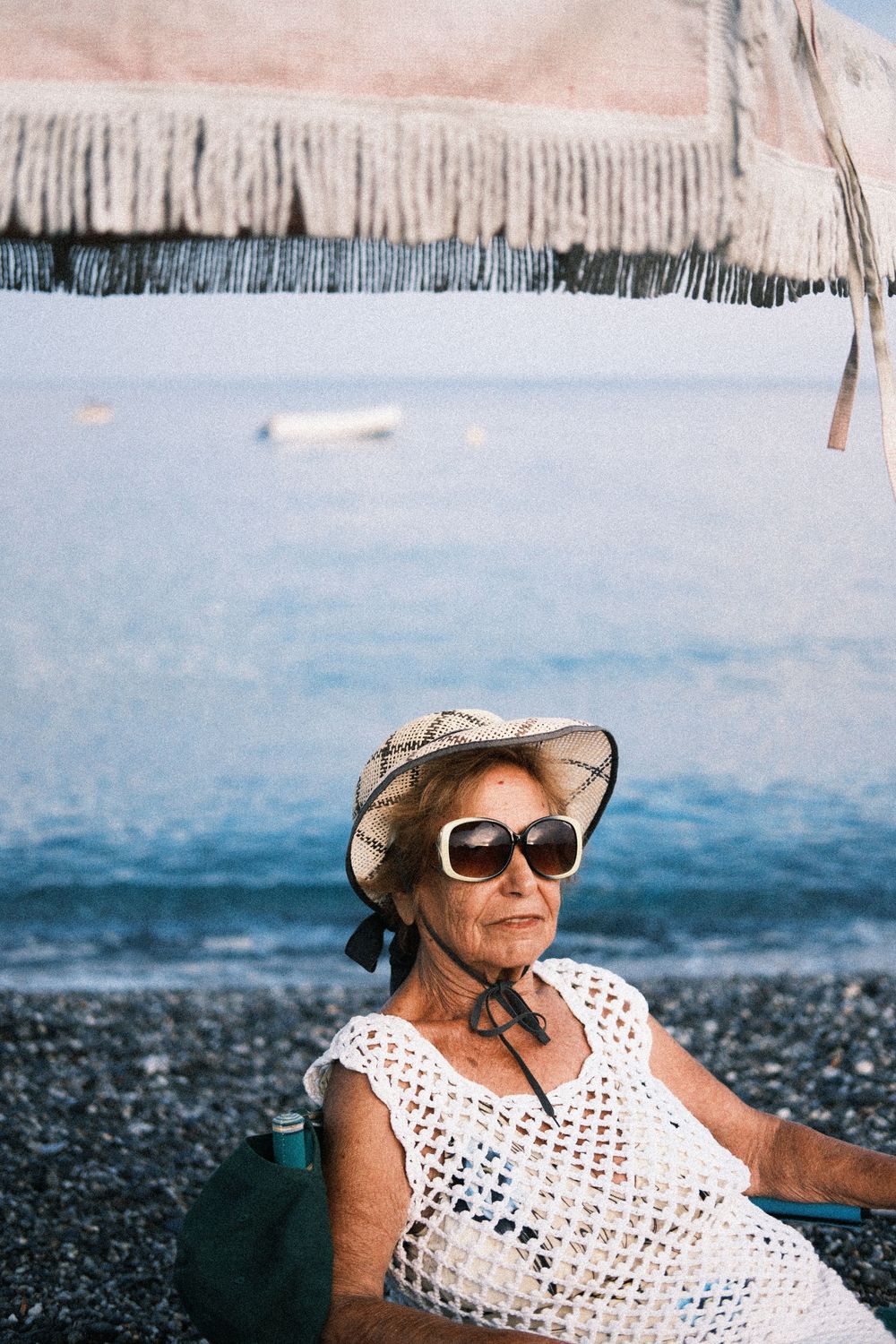A person wearing sunglasses and a white crochet top relaxes on a dark beach near the ocean.