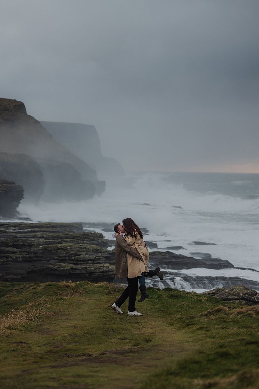 Cinematic engagement session at Cliffs of Moher during dramatic coastal storm at sunset
