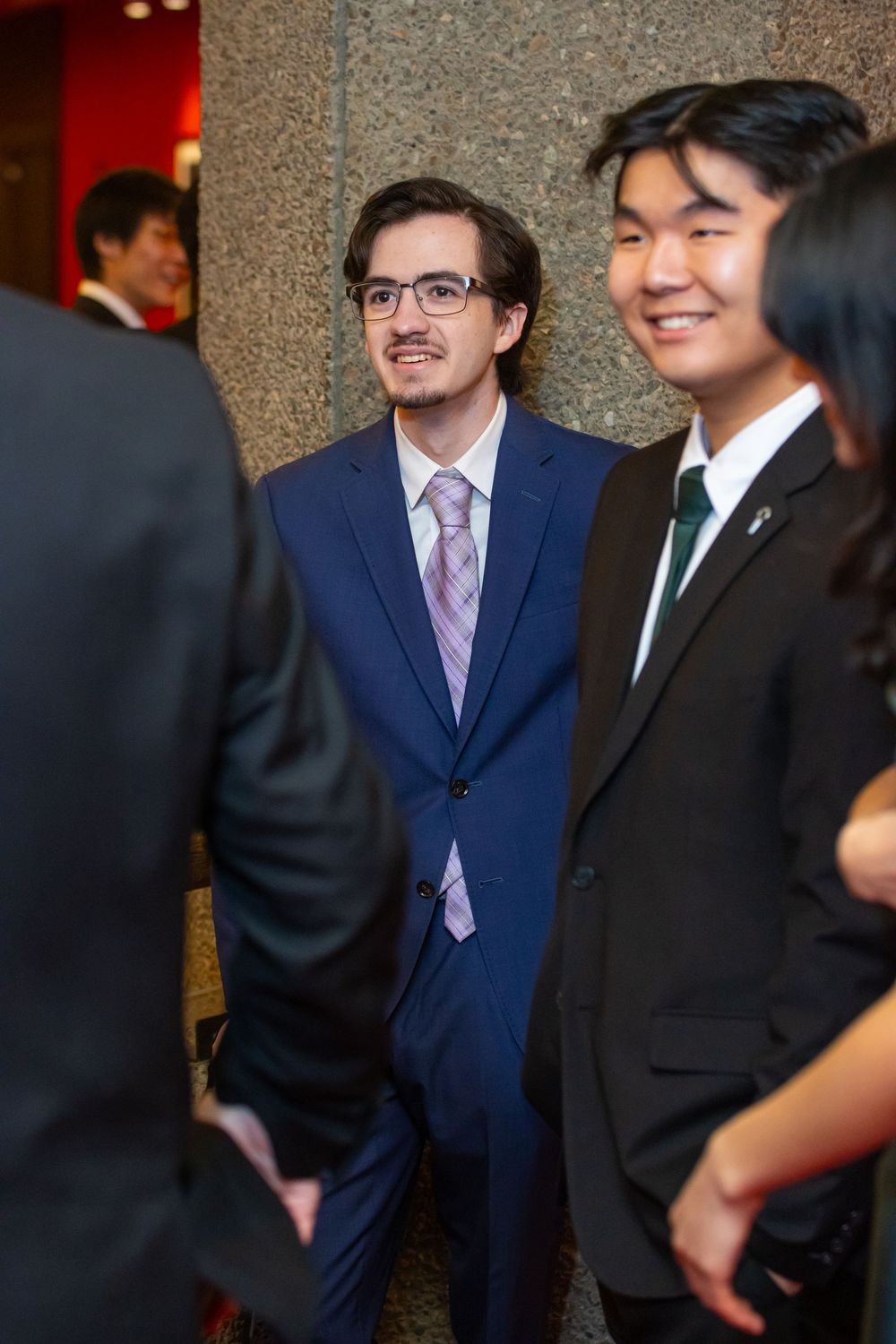 Professional event attendees in formal business attire engage in conversation at an indoor gathering.