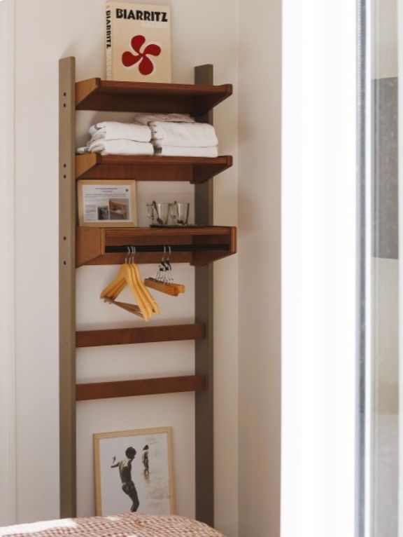 Modern wooden wall-mounted coat rack with multiple hooks and shelves for storage in a bright white hallway.