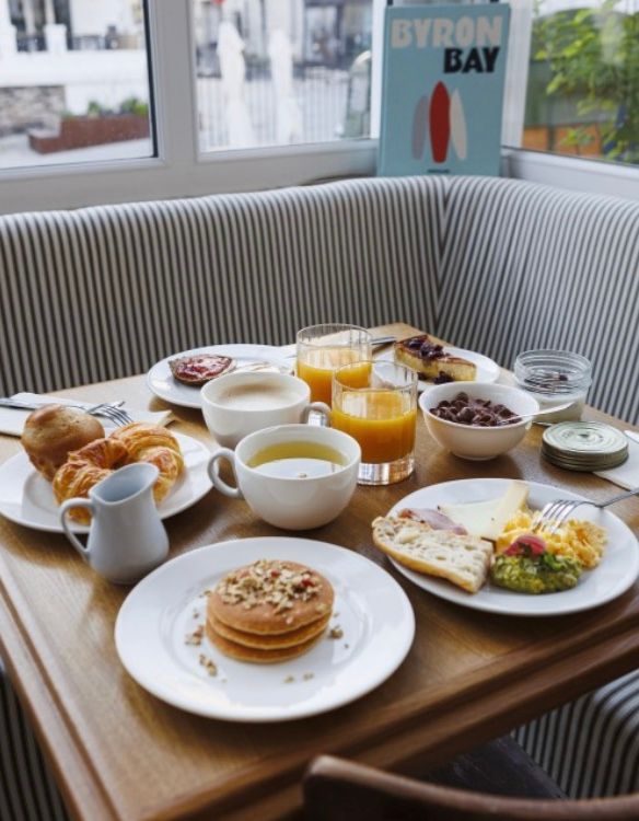 A series of breakfast plates on wooden trays with pastries, juice, and coffee arranged on a striped couch.