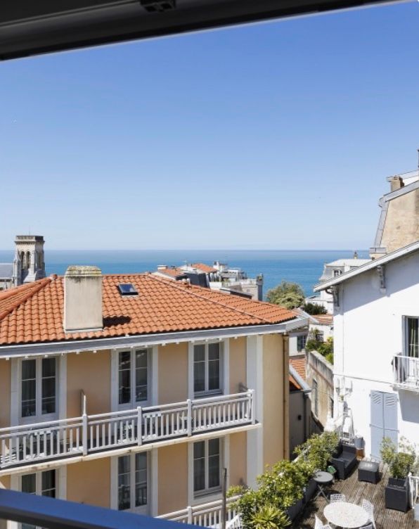 Mediterranean coastal town view with terracotta roofs and white buildings overlooking the blue ocean on a sunny day.