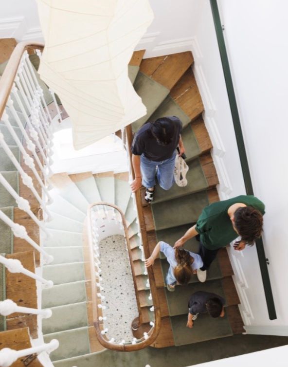 People walking down a white spiral staircase with wooden steps viewed from above in a modern building.