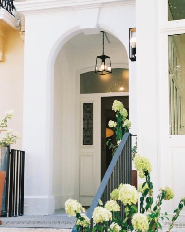 White arched entryway with black lantern and hydrangea flowers blooming in front of Mediterranean style home.