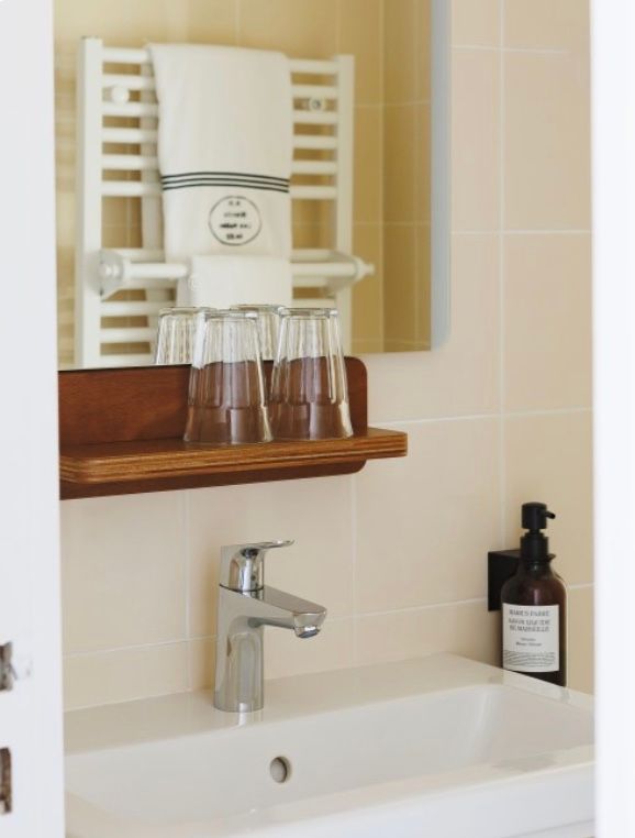 Modern bathroom interior with white towel rack, glass shelf, and chrome fixtures mounted on beige tiled wall.