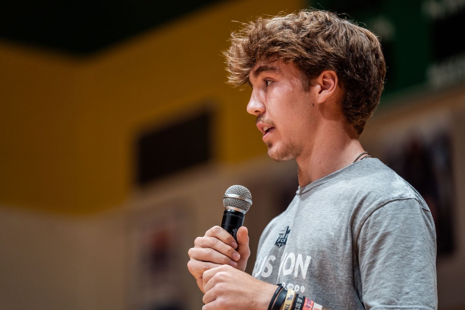 A performer speaks into a microphone while wearing a gray t-shirt during a live performance.