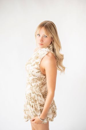 Young blonde woman in a gold and white floral halter dress posing sideways in a white studio.