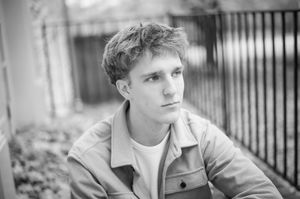 Black and white portrait of a young man in a jacket gazing thoughtfully outdoors.