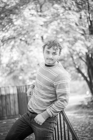 Black and white portrait of a curly-haired teen in striped sweater leaning on a railing outdoors.