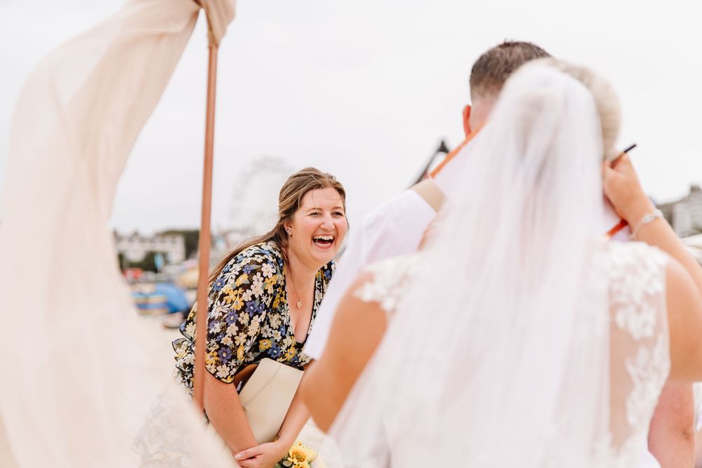 UK beach wedding on Weymouth Beach with Ceremonies by Laura Bell. Celebrant laughs at bride and groom. Sunflower wedding bouquet