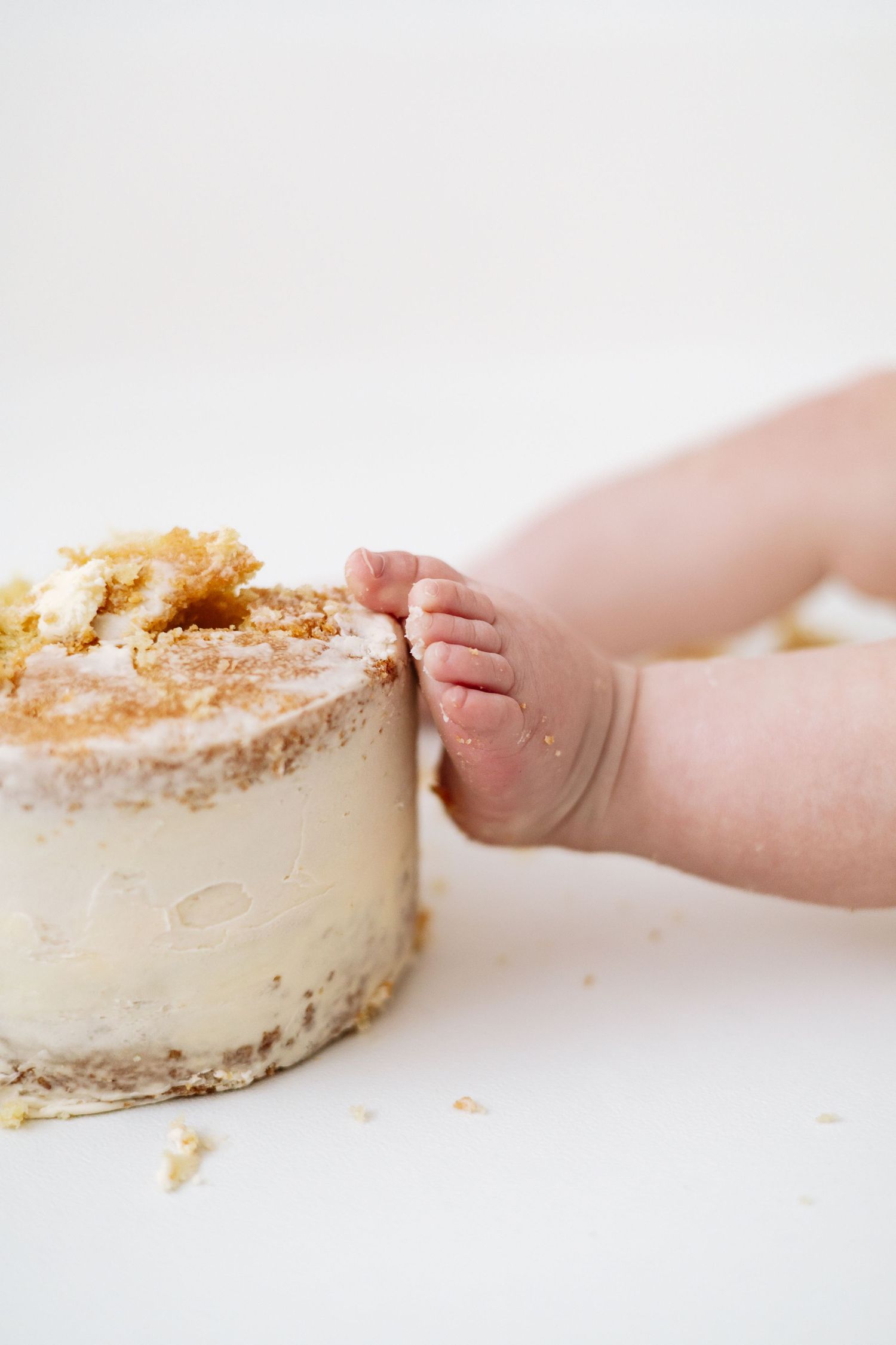 Tiny baby foot next to a white frosted cake with crumbs on top against light background during Birthday shoot based in Nottingham